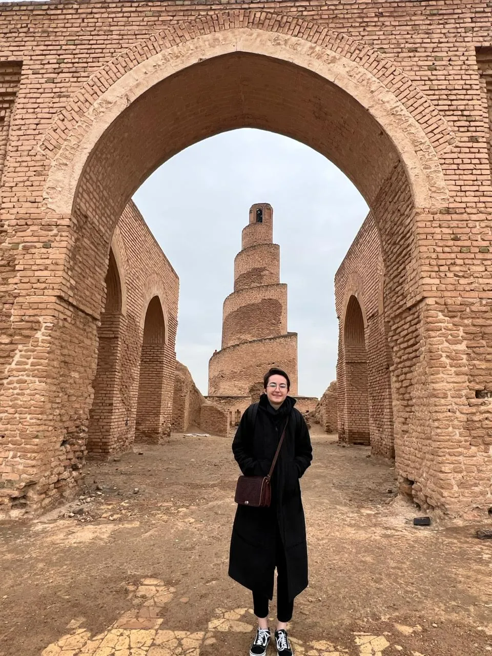 The spiral Malwiya minaret of Samarra framed through a ruined brick arch of the Great Mosque's enclosure wall.